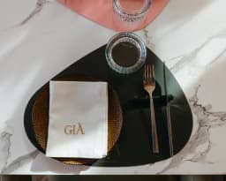 Servilleta con el monograma GIÀ bordado en hilo dorado sobre bajoplato negro