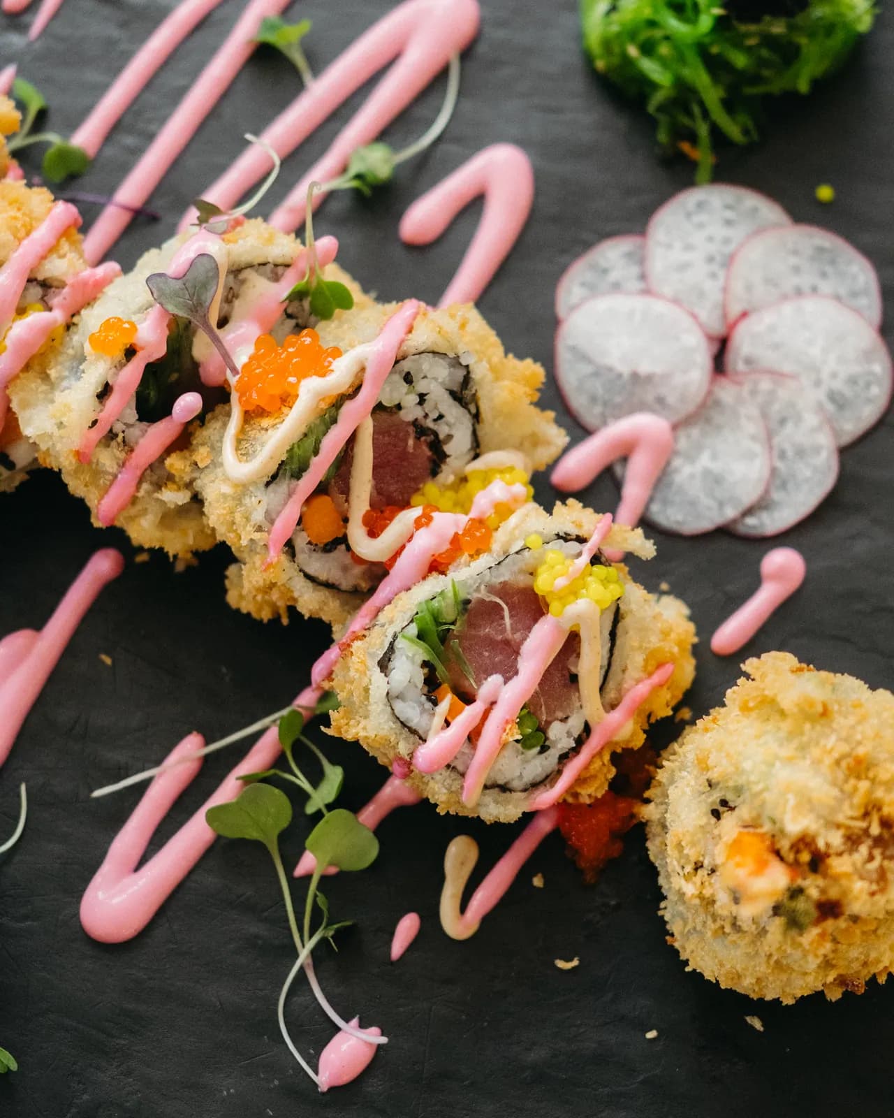 Detalle de un entrante contemporáneo con drizzle rosa, caviar y micro hierbas sobre slate negro