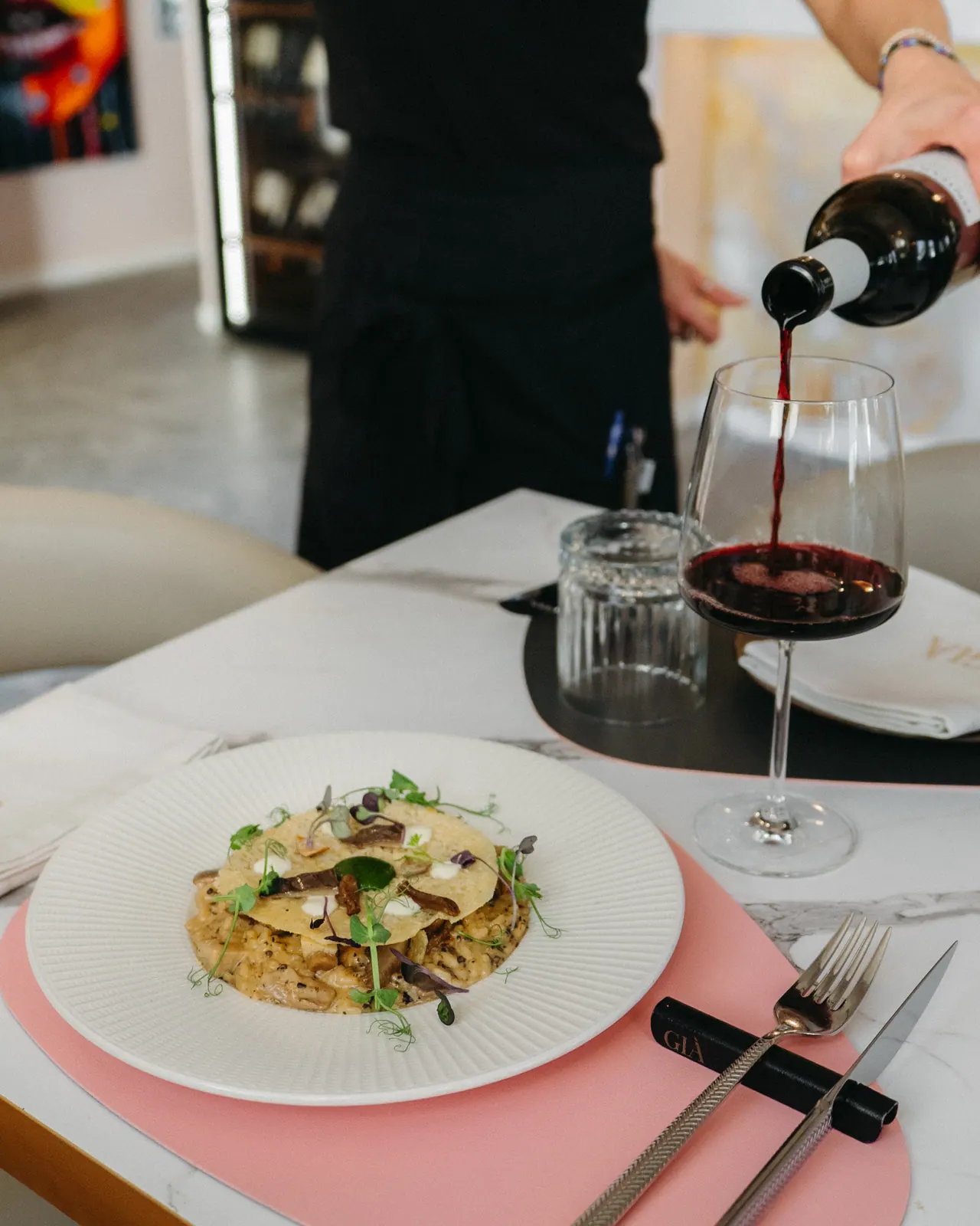 Pasta scialatielli servida con vino tinto italiano siendo descorchado · mantel rosa palo y mármol