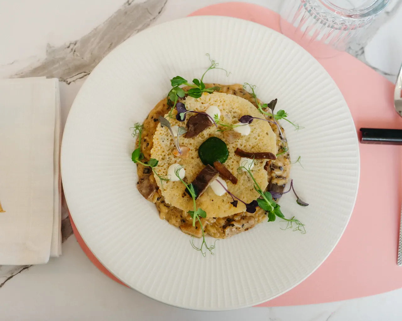 Tortello Già mit knuspriger Tuile, Pilzen und Mikrokräutern · Vogelperspektive auf altrosa Tischwäsche und Marmor